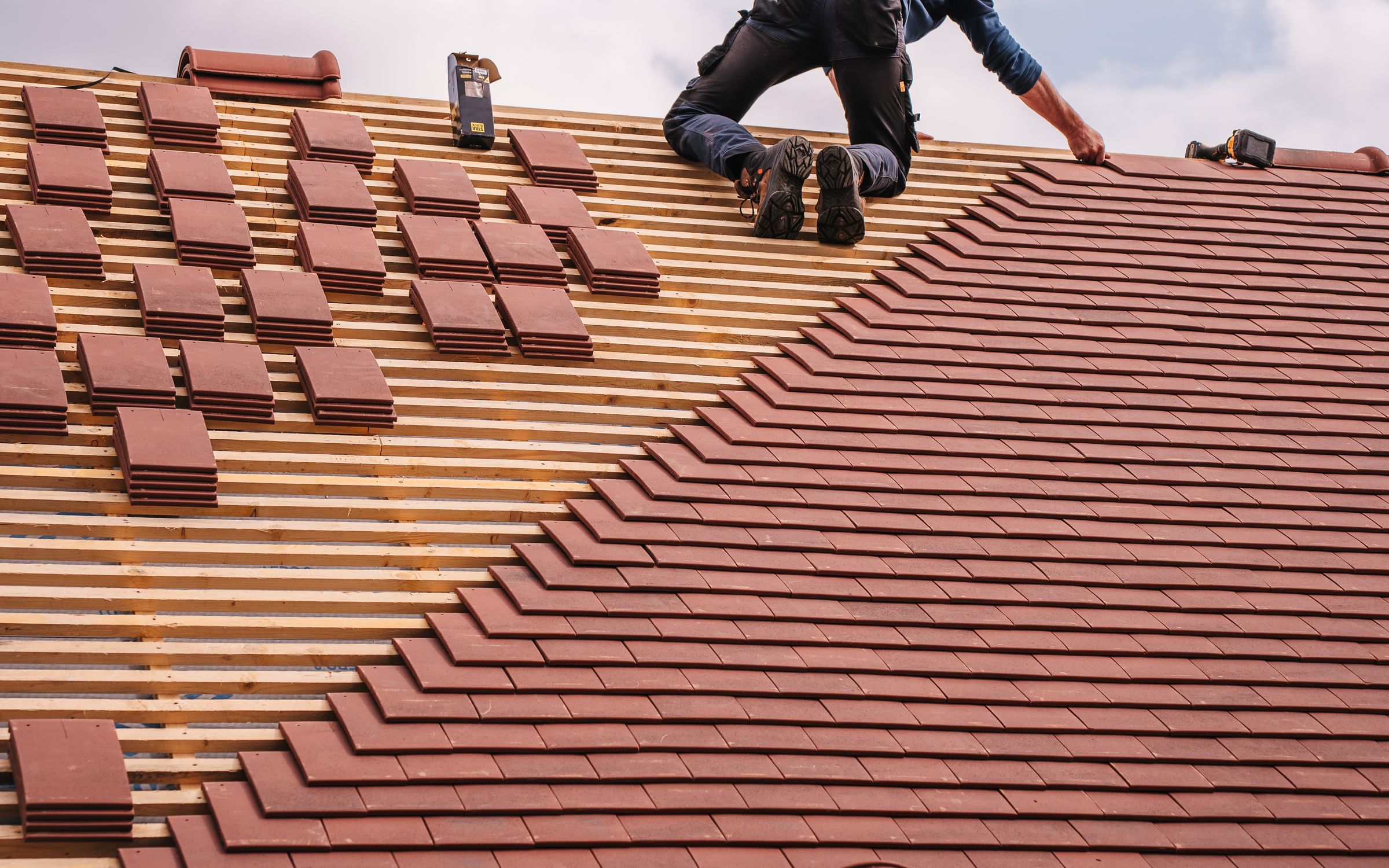 Couvreur posant des tuiles en terre cuite sur une toiture en cours de rénovation